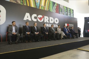 Homens em cima de palco sentados em cadeiras de forma enfileirada, à frente de um banner escrito Acordo Paulista