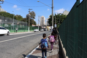 crianças com mochilas nas costas caminham em direção à escola em uma rua de São Paulo