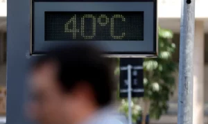 Homem passando diante de termômetro de rua indicando temperatura de 40 graus