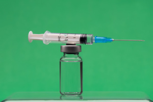 frasco de medicamento e seringa à frente de fundo verde