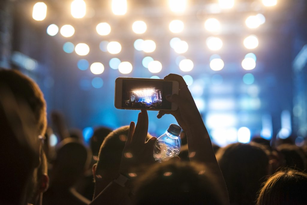 Pessoa em plateia de show ergue o celular para filmar o palco