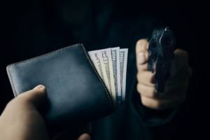 homem apontando arma para outro, que entrega carteira com dinheiro