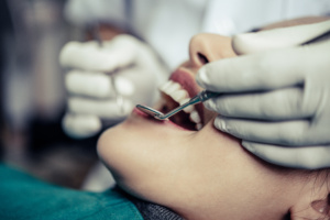 Dentista em consultório odontológico tratando boca de paciente.