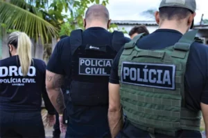 Três policiais civis do Amazonas (uma mulher e dois homens) de costas