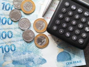 notas de 100 reais, moedas, calculadora e caneta
