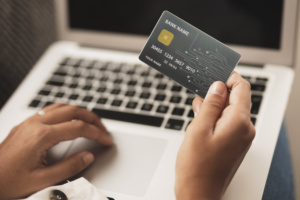 pessoa mexendo em laptop e segurando cartão de crédito