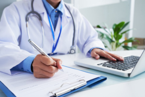 médico usando computador e fazendo anotações